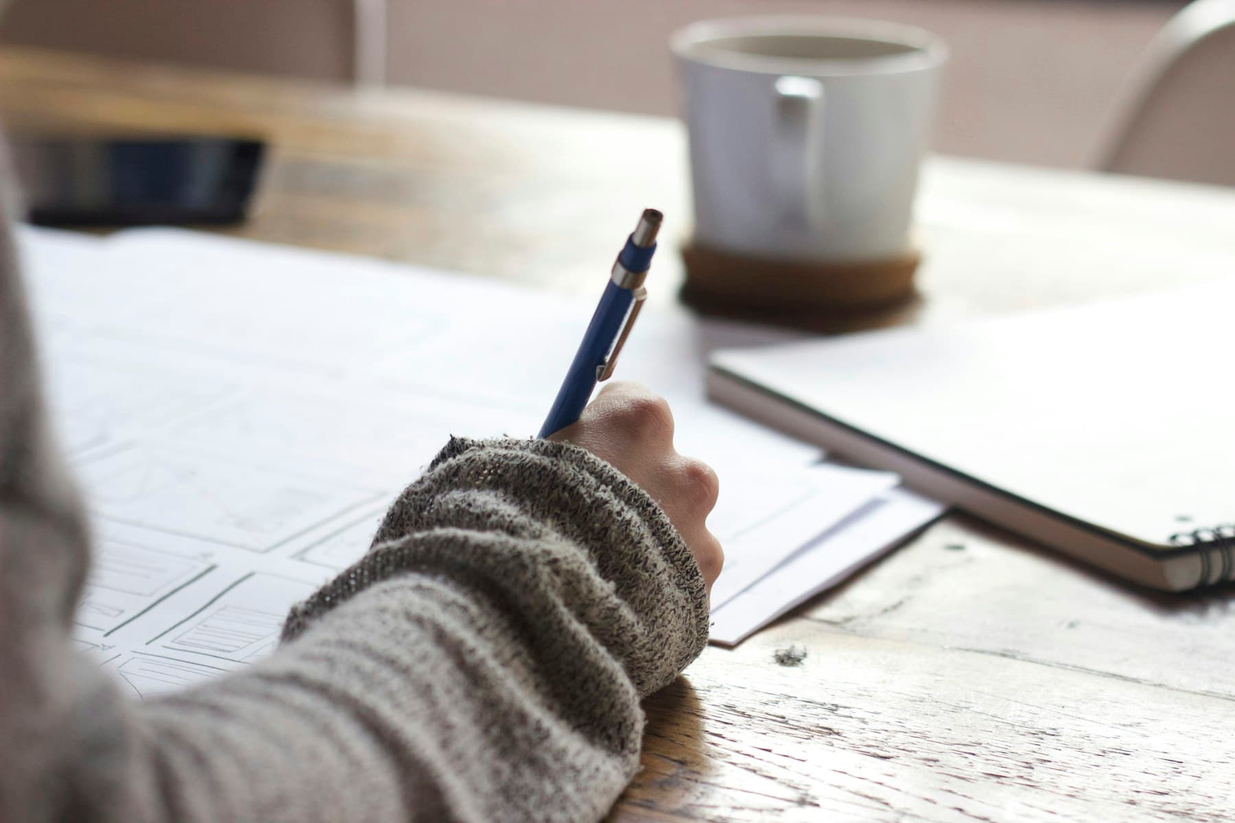 Hands resting beside an open notebook and pen on a bright desk, suggesting calm focus